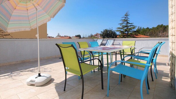Une terrasse extérieure avec une table et des chaises, un parasol à rayures et une vue sur les environs.