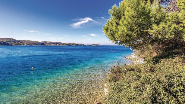Paisaje costero con mar azul cristalino, costa rocosa y vegetación exuberante.