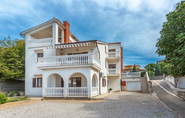 A two-story building with a white facade, multiple balconies, and a gravel driveway. - Beautiful apartment in Omisalj with WiFi (Omisalj)