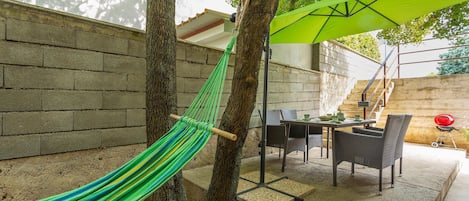 A hammock between trees, a patio table with chairs, and a barbecue grill.