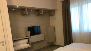 A hotel room with a bed, a TV mounted on a wall, a wardrobe, and a window with curtains. - Holiday apartment mit Terrasse (Tignale)