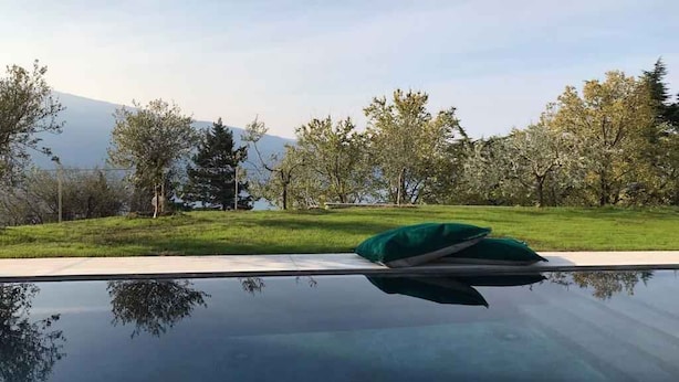 A pool with a green cushion on the edge, surrounded by a grassy area and trees. - Holiday apartment mit Terrasse (Tignale)