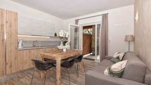 A modern kitchen with a wooden table and chairs, a coffee maker, and a vase of flowers. There is a grey sofa with cushions and a lamp in the living area. - Holiday apartment mit Terrasse (Tignale)