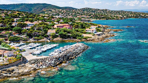Un pueblo costero con un puerto deportivo, costa rocosa y casas con balcones a la vista.