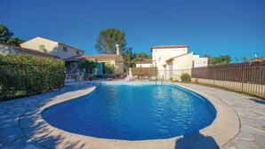 Una piscina con borde curvo, rodeada por un patio de piedra y una cerca.
