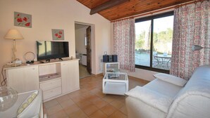 Una sala de estar con televisor, sofá, lámpara y ventana con cortinas.