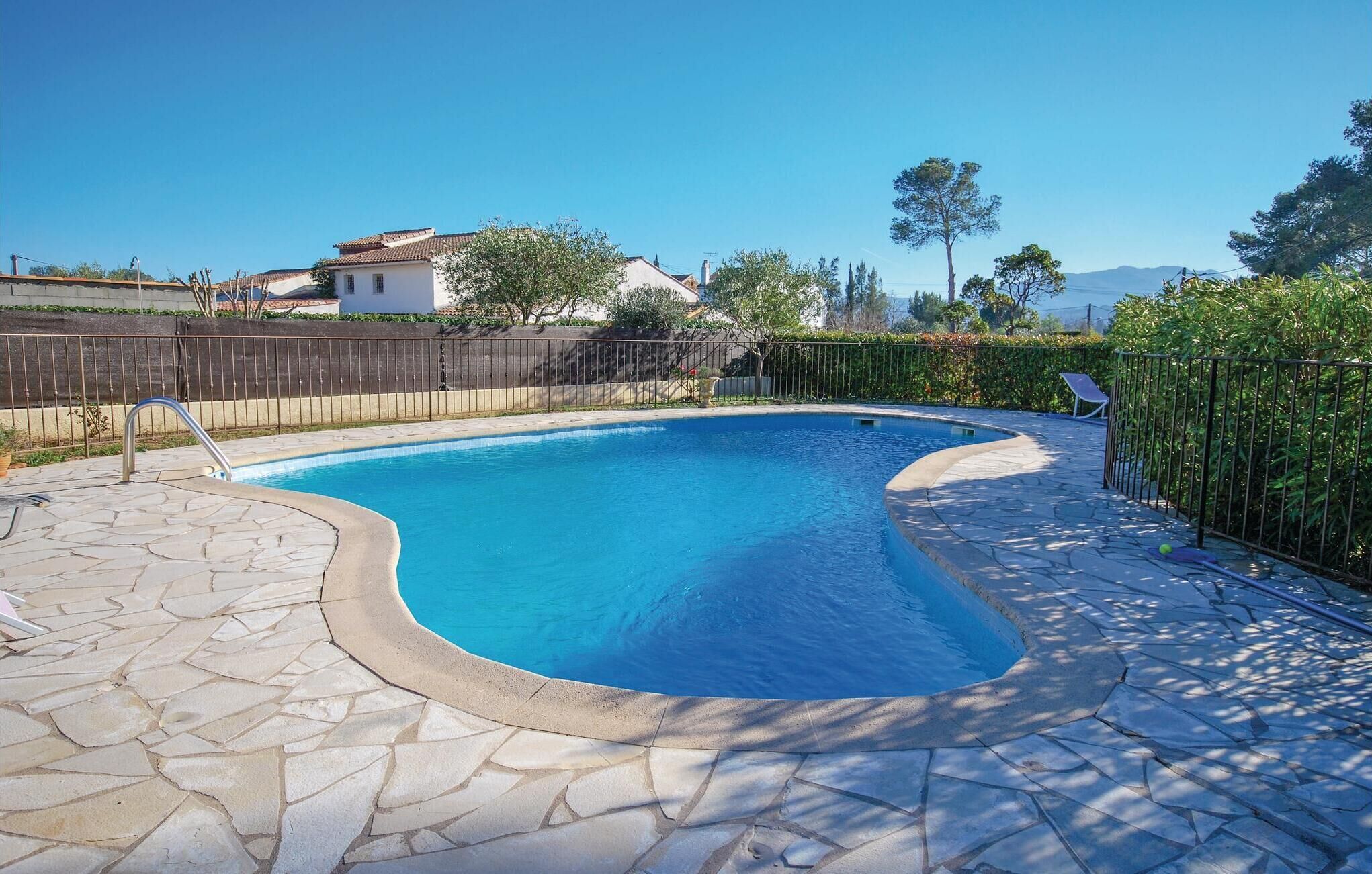 A swimming pool with a stone deck, surrounded by a wooden fence and greenery.