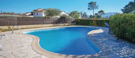 A swimming pool with a stone deck, surrounded by a wooden fence and greenery.