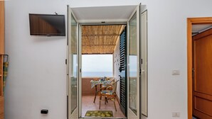 A room with a view of the sea, a dining area with a table and chairs, and a television mounted on the wall.