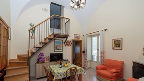 A spacious living area with a staircase, a dining table with chairs, a sofa, and a television.