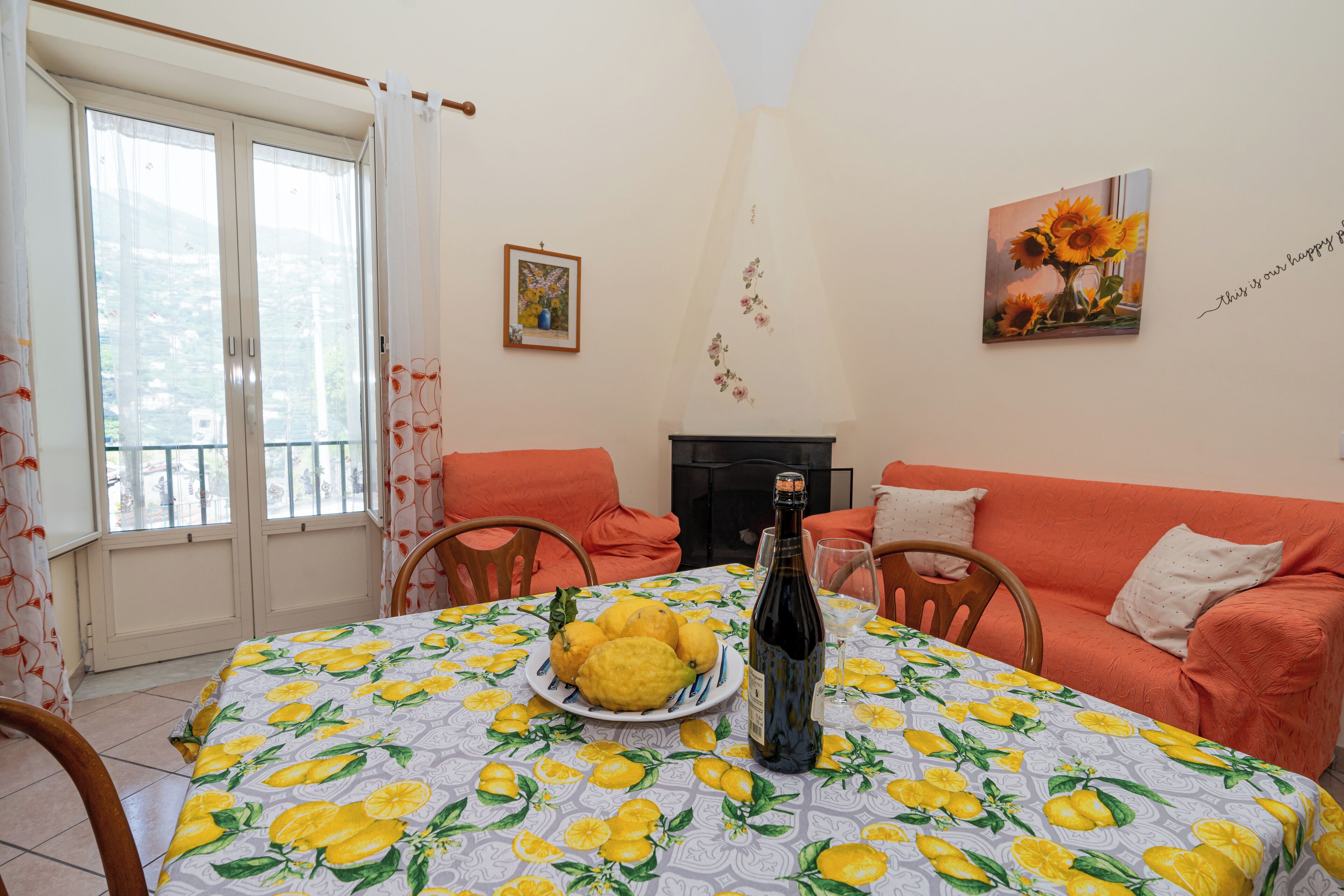 Un rincón de comedor con una mesa dispuesta para dos personas, que incluye un plato de limones y una botella de vino.