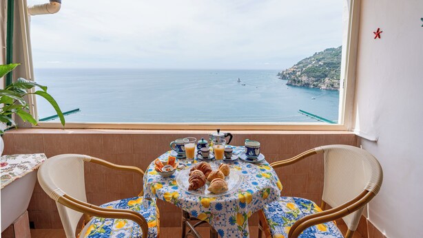 A balcony with a table set for breakfast, overlooking a coastal view.