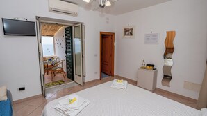 A hotel room with a bed, a desk, a chair, a TV, and a door leading to a balcony.
