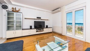 Una sala de estar moderna con televisor, armarios, una mesa de centro de vidrio y vistas al mar.