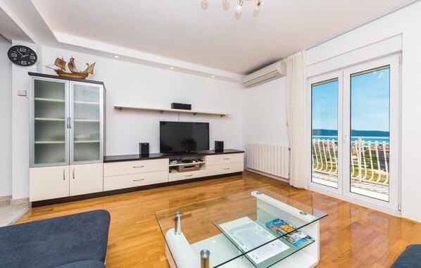 Un salon moderne avec un téléviseur, des meubles de rangement, une table basse en verre et une vue sur la mer.