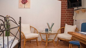 A room with a bed, two wicker chairs, a small table with a lamp, and a television on the wall.
