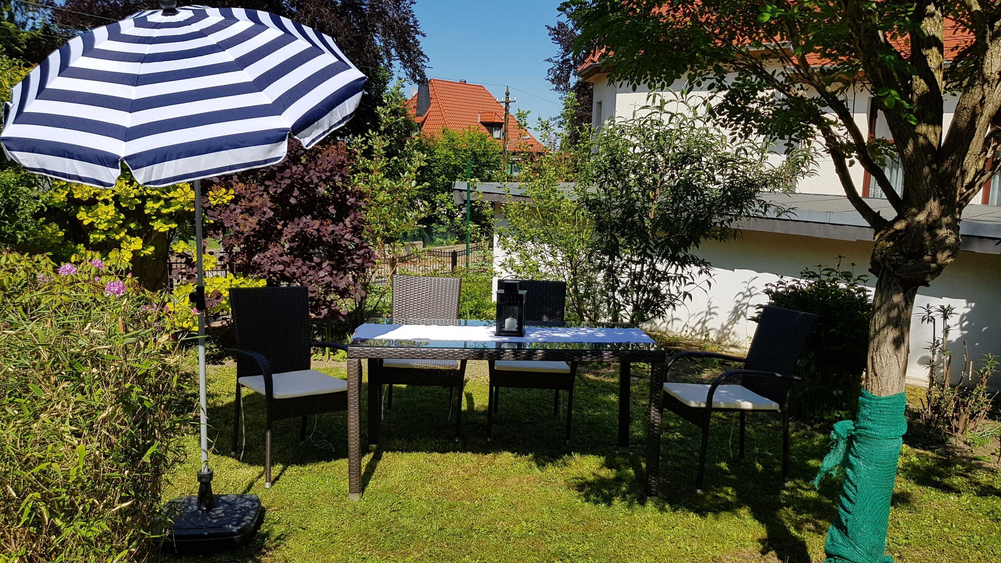 An outdoor patio with a table and chairs, a striped umbrella, and a garden with various plants.