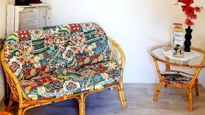 A room with a wicker sofa, a small round table with a vase, and a framed picture on the wall. - Apartment Sandra Mattaj (Blankenburg (Harz))