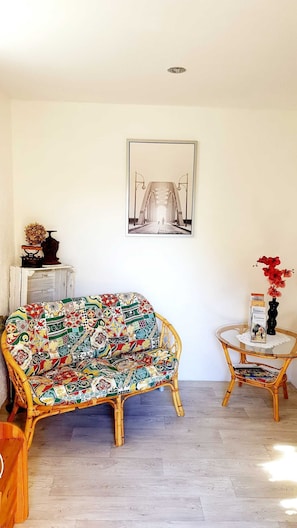 A room with a wicker sofa, a small round table with a vase, and a framed picture on the wall. - Apartment Sandra Mattaj (Blankenburg (Harz))