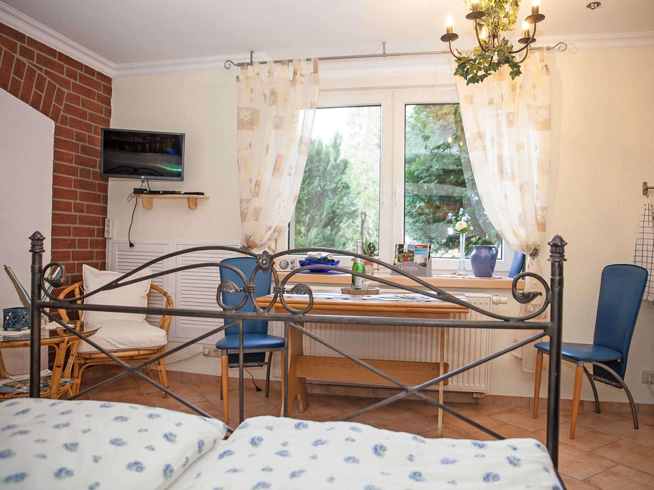 A room with a bed, two chairs, a desk with a computer, and a window with curtains.