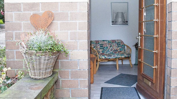 A doorway leading to a room with a wicker basket of plants, a patterned bench, and a framed picture on the wall. - Apartment Sandra Mattaj (Blankenburg (Harz))