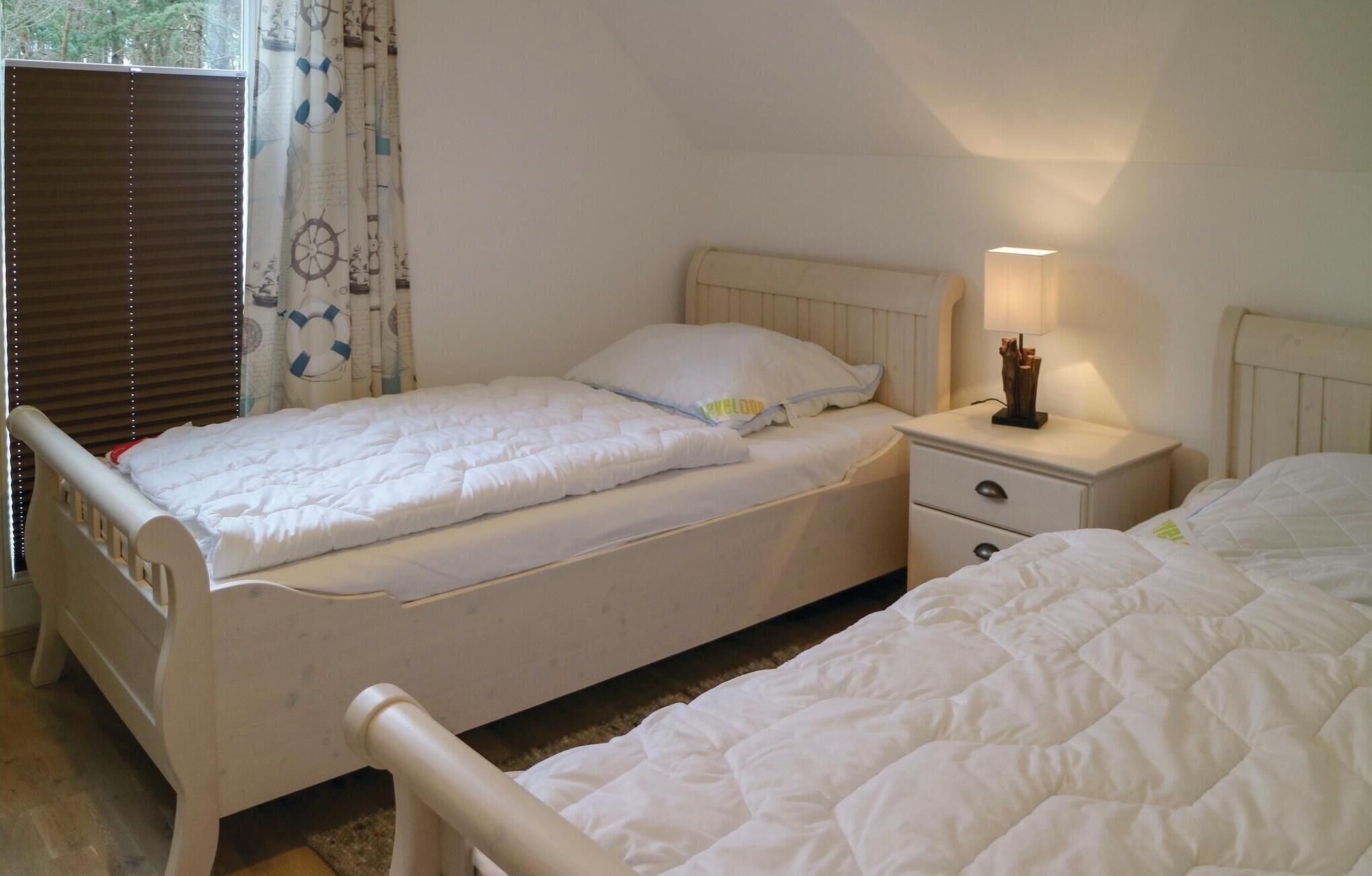 A bedroom with two single beds, a bedside table with a lamp, and a window with blinds.