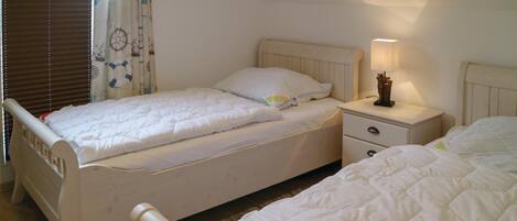 Un dormitorio con dos camas individuales, una mesita de noche con lámpara y una ventana con persianas.