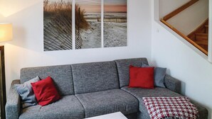 A grey sofa with red and blue cushions, a white table, and a beach scene painting on the wall. - Gorgeous home in Breege/Juliusruh (Breege/Juliusruh)