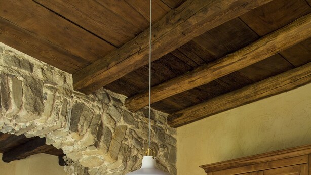 Un comedor rústico con una mesa de madera dispuesta para dos, un arco de piedra y un mueble de madera con puertas de cristal.