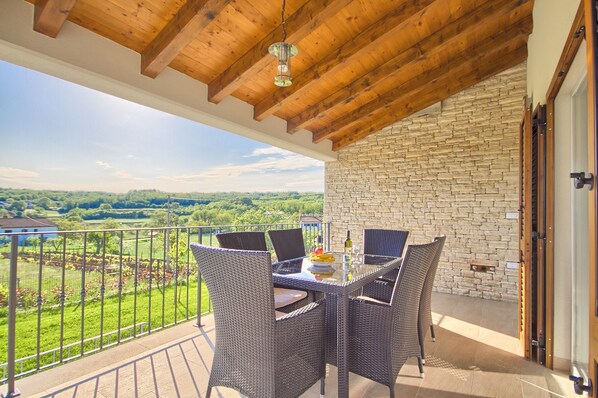Un balcon agrémenté de meubles en osier, une table avec une bouteille et des verres, et une vue sur la verdure et les bâtiments.