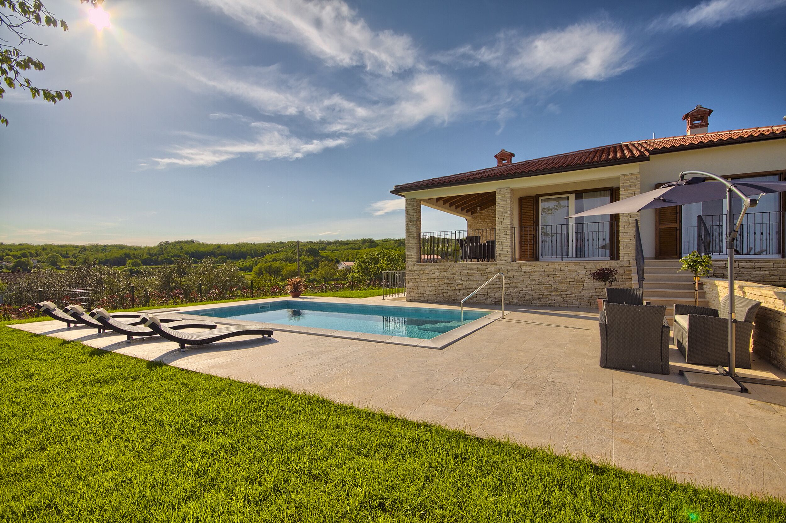 Ein Poolbereich mit Liegestühlen, einer überdachten Terrasse und Blick auf die umliegende Landschaft.