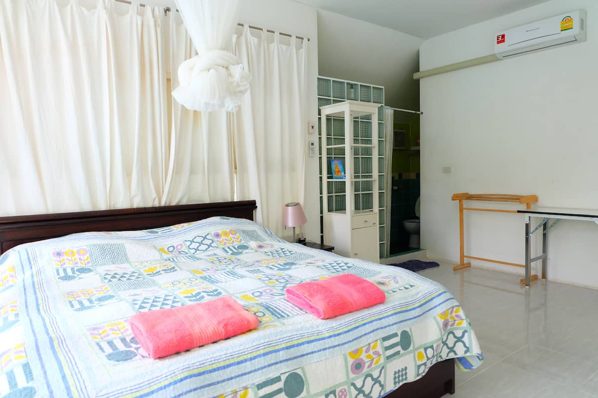 A bedroom with a bed, a nightstand, a lamp, a wardrobe, and an air conditioning unit.