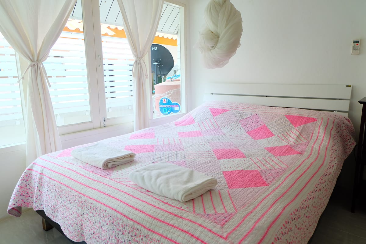 A bedroom with a bed, curtains, a hanging light, and a window with blinds.