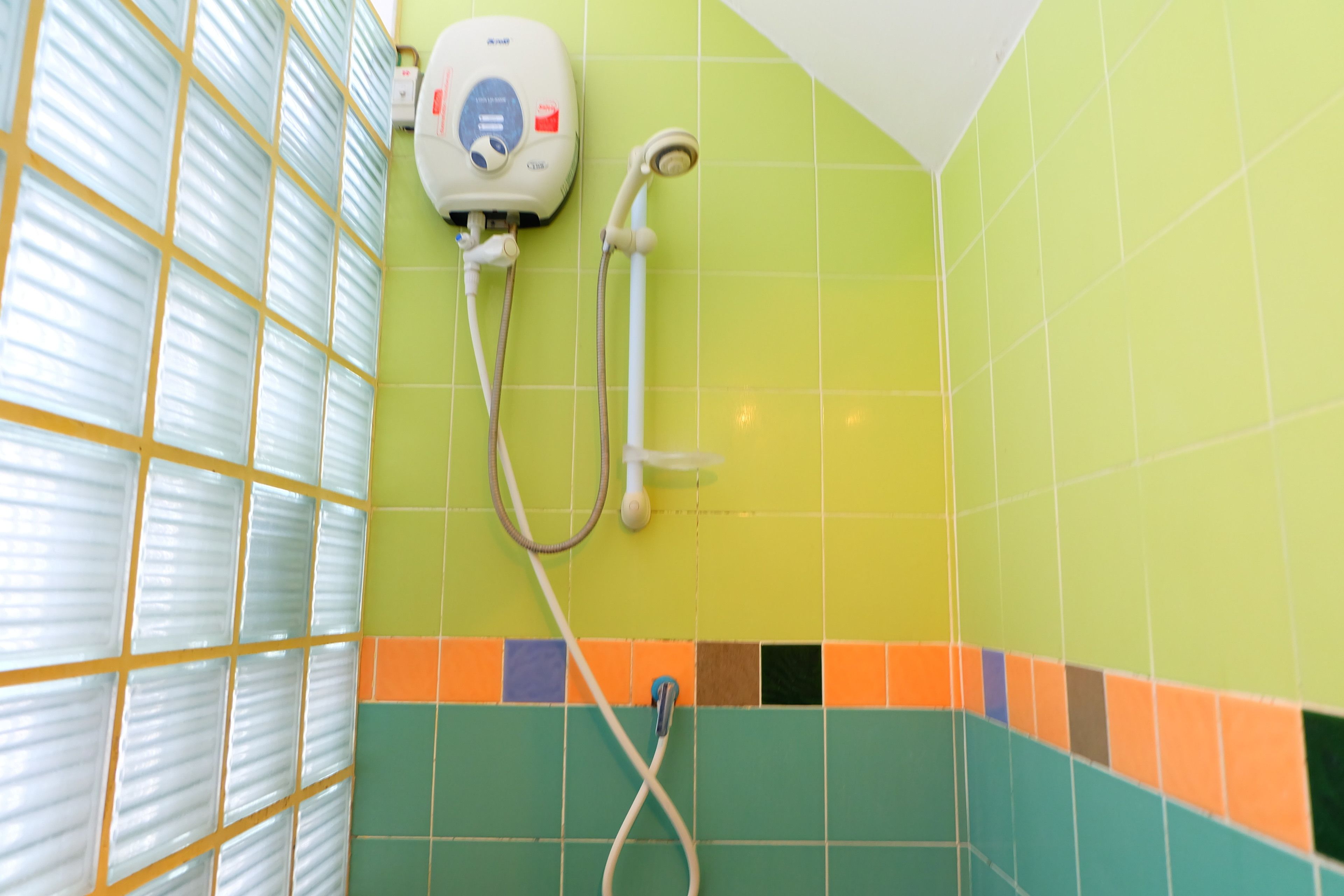 A bathroom with a shower, a hand dryer, and a tiled wall with a multicolored pattern.