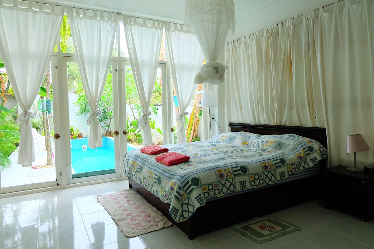 A bedroom with a bed, curtains, a nightstand, and a view of a swimming pool.