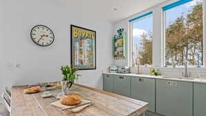 Une cuisine moderne avec une table en bois, une horloge, une affiche encadrée et une fenêtre donnant sur des arbres.