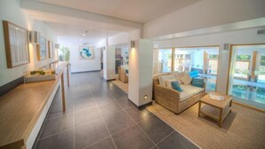 Un hall d’hôtel moderne comprenant un comptoir d’accueil, un espace salon avec un canapé et des fauteuils, et une grande fenêtre donnant sur une piscine.