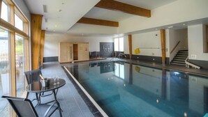 Une piscine intérieure avec un mur en verre, une table avec des chaises et un escalier.
