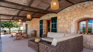 An outdoor seating area with wicker furniture, a wooden table, and hanging lights.