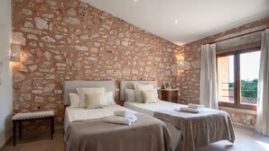 A room with two beds, stone walls, a bench, and a window with curtains.