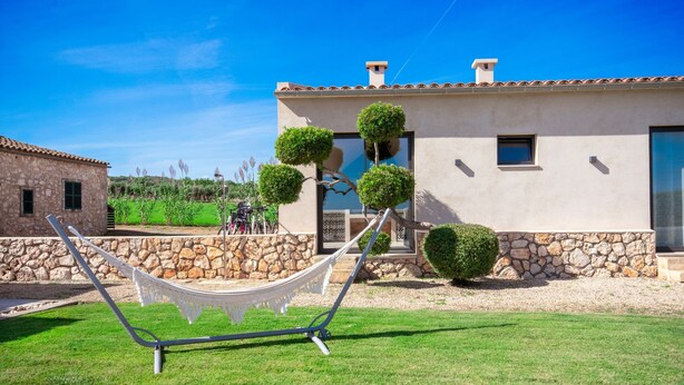 A modern house with a stone facade, a hammock in the yard, and neatly trimmed bushes.