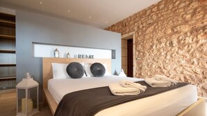 A modern bedroom with a stone wall, a bed with white linens, a dark throw blanket, and a sign above the bed that reads "REMAX". - 44287 Finca Rústica Sa Pleta - 44287 Finca Rústica Sa Pleta (Manacor)