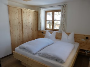 Quarto com cama de madeira, janela com cortinas e guarda-roupa de madeira.