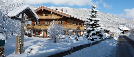 A wooden chalet with balconies, a snow-covered landscape, and a mountain in the background.