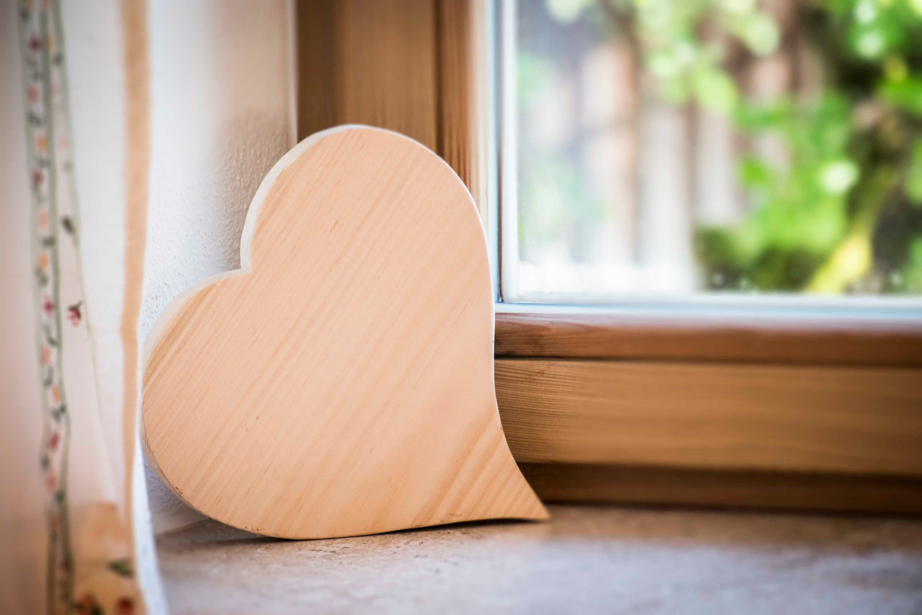 Un objet en bois en forme de cœur, appuyé contre le rebord d’une fenêtre.