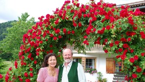 A couple standing in front of a house with a large red rose bush arching over them. - Vacation apartment 4 Resi - Guesthouse Becher, Kreuth-Point (Kreuth)