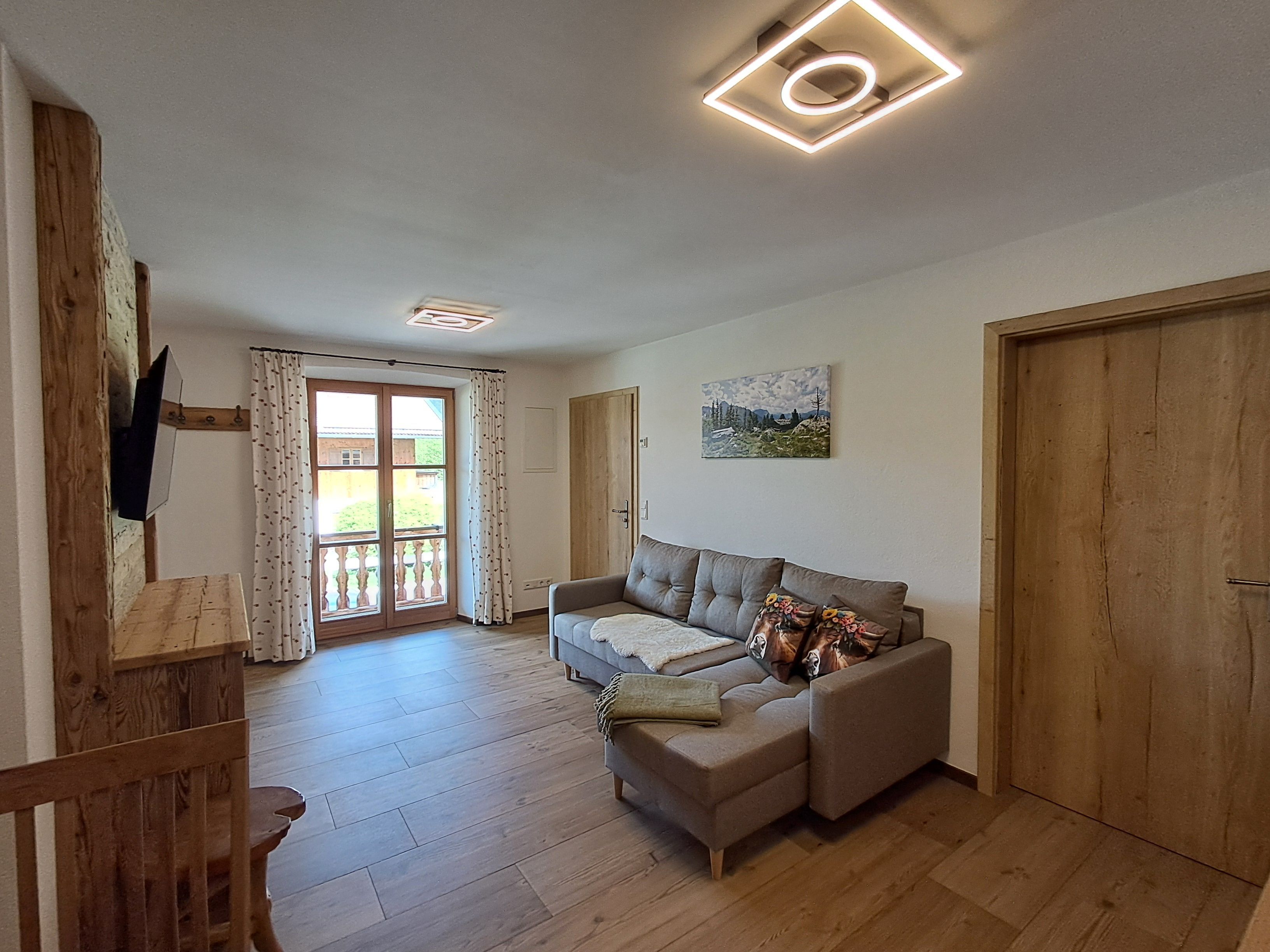 A living room with a sofa, a wooden floor, a painting on the wall, and a door.
