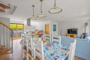 Ein modernes Wohnzimmer mit einem blauen Sofa, einem Esstisch mit Stühlen, einer Küchenzeile und einer Treppe.