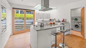 A modern kitchen with a central island, stainless steel appliances, and a view of a garden through glass doors. - Beautifully decorated "Sea Shack", with large sun roof terrace and large private hot tub. (Looe)