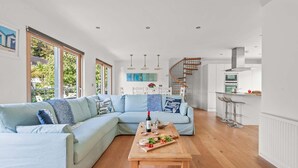 A modern living room with a light blue sectional sofa, a wooden coffee table, and a kitchen area with a built-in oven and bar stools. - Beautifully decorated "Sea Shack", with large sun roof terrace and large private hot tub. (Looe)
